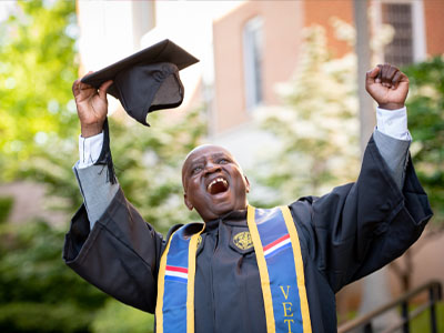 A recent graduate holds his cap in celebration, shouting in excitement.