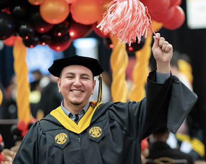 A male student celebrating with graduation cap and gown.